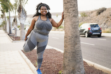 Curvy african woman stretching during workout routine outdoor at city park - Focus on face