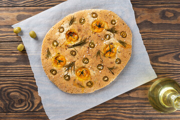 Vegan focaccia with olives, tomatoes, rosemary and spices on a wooden table. Horizontal orientation, top view.