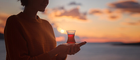Woman drinking turkish tea from traditional turkish teacup and enjoys panorama over sunset of Kas...