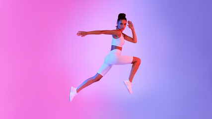 Fototapeta na wymiar Athletic Female Jumping In Mid-Air Over Pink And Blue Background