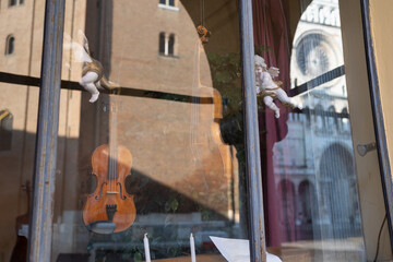 Store Window of a Luthier's Shop: Handmade Violins on Display  and Reflection of the Cathedral of Cremona in the Shop Window, Italy - obrazy, fototapety, plakaty