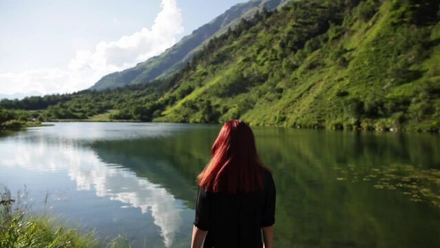 beautiful Girl in black with short red hair goes to the mountain lake - view from the back - 4 takes