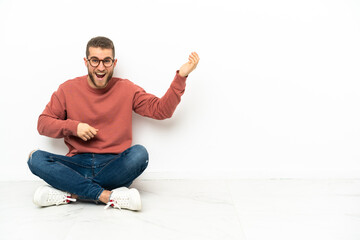 Young handsome man sitting on the floor making guitar gesture