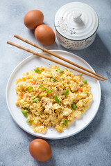 Egg fried rice served on a white plate, vertical shot on a light-blue stone background, elevated view