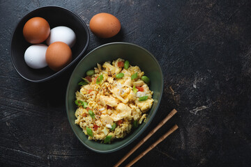 Bowl of chinese-style egg fried rice on a dark-brown stone background, horizontal shot with space, view from above