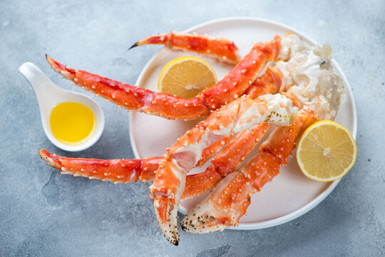 White plate with kamchatka crab claws, lemon and butter, horizontal shot on a light-blue stone background