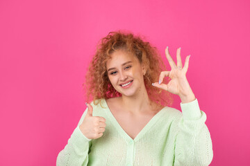 Young beautiful curly red-haired girl shows ok sign to the camera. A sign of success and good luck.