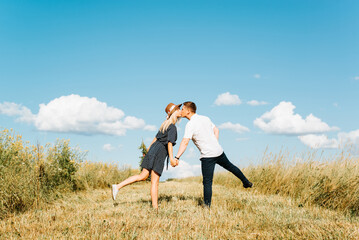 Romantic date, valentine's day, love story concept. Young caucasian couple in love kissing in field on sunny summer day, outdoors. Back view of flirting man and woman holding hands together in meadow