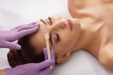 Beautician is removing hair from beautiful female face with hot wax. Woman has a beauty treament...