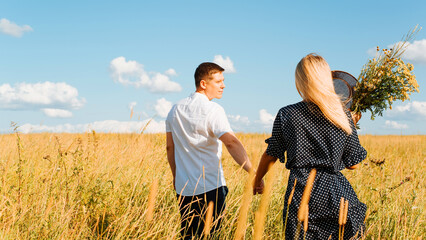 Beautiful caucasian couple in love holding hands in meadow on walk on sunny summer day outdoors. Back view of young family having romantic time together in nature. Valentine's day, love story concept