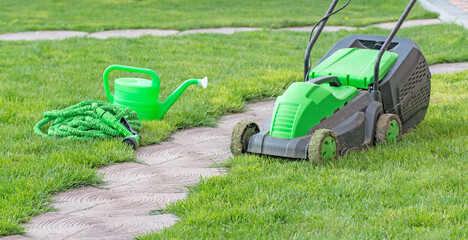 gardening tools concept. Gardening equipment, lawnmower, saw, green watering can, garden plants in pots in the garden