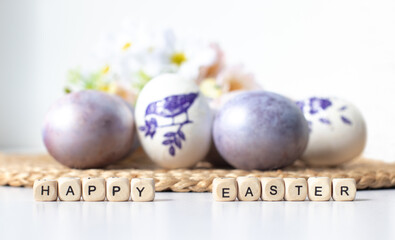 Easter concept. Purple eggs on a straw cloth and wooden letters happy Easter