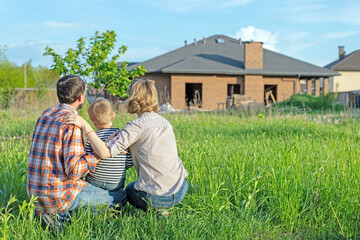 Back view of happy family is standing near their new modern house and hugging