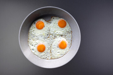 Four fried eggs in a round frying pan on a gray background.