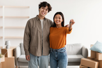 Fototapeta na wymiar Portrait of young happy Asian couple holding house key, posing in apartment with carton boxes. Moving day concept