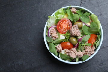 Bowl of delicious salad with canned tuna and vegetables on black table, top view. Space for text