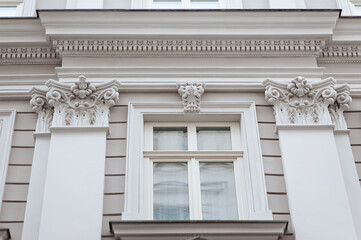 Window with wooden frame. Neoclassical building with a complex structure with pilasters and capitals in the Corinthian style. Light gray facade of an old house in Lviv, Ukraine.
