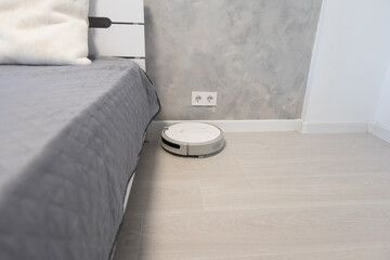 Robotic vacuum cleaner on laminate wood floor in bedroom.