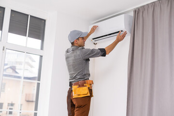 Obraz premium Young Man Repairing Air Conditioner Standing On Stepladder