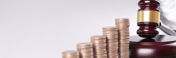 Judge wooden gavel lying near piles of coins in ascending order closeup