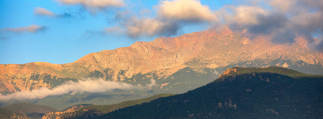 Panoramic image of sunrise striking Pikes Peak in Colorado as low lying clouds hover near the mountain