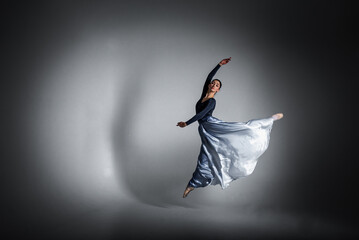 young pretty, fragile, beautiful ballerina dancing in a long blue dress on a uniform background,...