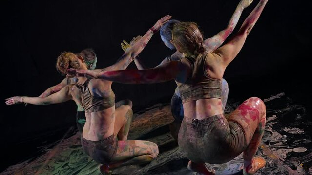 women stained with paints are dancing in dark studio, contemporary dance and art performance
