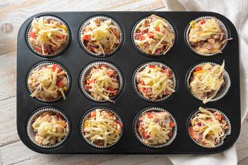 Baking tray with prepared hearty pizza muffins from yeast dough, tomatoes, vegetables, sausage and...