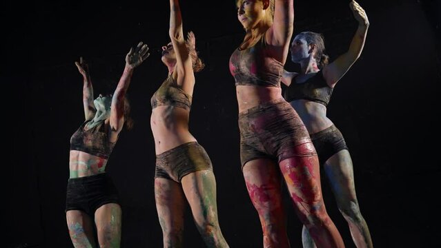 young sexy ladies covered by dyes are dancing, modern choreography in dark studio