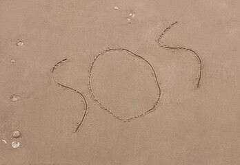 SOS distress signal text written on sand background 