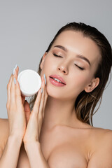 young woman with wet hair and closed eyes holding cosmetic cream isolated on grey.