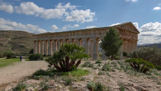 Doric temple of Segesta behind the trees at sunny spring day in Sicily, Italy with unrecognizable tourists