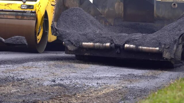 A team of workers is laying hot asphalt on the railway tracks of a street-long term care. Road construction workers with shovels in protective uniforms take asphalt from the body with shovels.