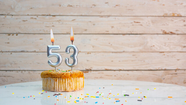 Happy birthday greetings for 53 years of silver numbers on the background of white boards copy space. Beautiful birthday card with a muffin with a burning candle for fifty-three years