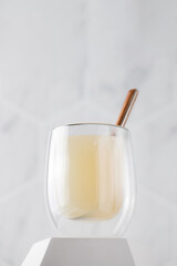 Healthy bone broth in a transparent mug on a pedestal with a spoon on a light background.