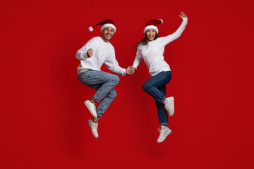 Crazy Sales. Excited Young Couple In Santa Hats Jumping Over Red Background
