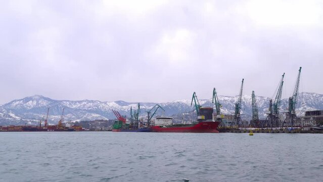 BATUMI, GEORGIA - JANUARY 2022: ferry stands in port against backdrop of snow-capped mountains. Winter weather. concept of marine logistics. Cranes installed around perimeter. Containers are loaded