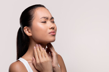 Asian woman suffering from sore throat, touching her neck