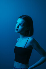 Fashionable portrait in the neon blue light of an attractive woman in a top, looking away with a...