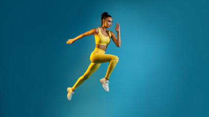 Motivated Young Lady Jumping Posing In Mid-Air Over Blue Background
