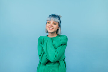 Portrait of a beautiful girl with blue hair with a smile on her face isolated on a blue background, looking at the camera.