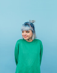 Cheerful teen girl with blue hair and in a green sweatshirt looks aside with a smile, isola on a blue background.vertical