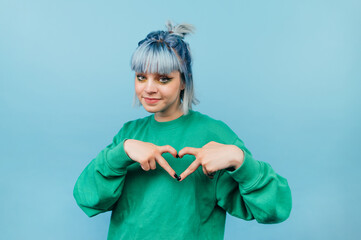 Beautiful teen girl in a green sweatshirt and colored waltz shows a heart gesture and looks at the camera with a smile on his face.