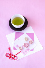 和紙の上の桜の干菓子と紅白の水引飾りと緑茶