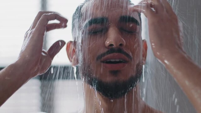 Sexy seductive arab bearded man in shower washing head showering in bathroom at home close up. Millennial brunette guy rinsing shampoo and conditioner from hair in warm bath hot water runs down face