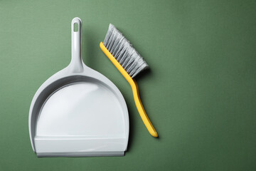 Plastic hand broom and dustpan on dark green background, flat lay. Space for text