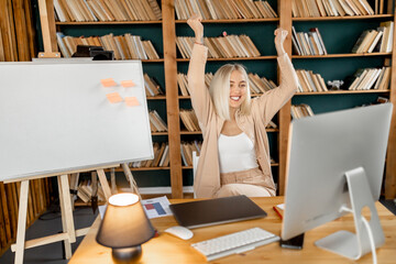 Overjoyed young businesswoman feeling euphoric about job promotion, smiling, sitting at the desk....