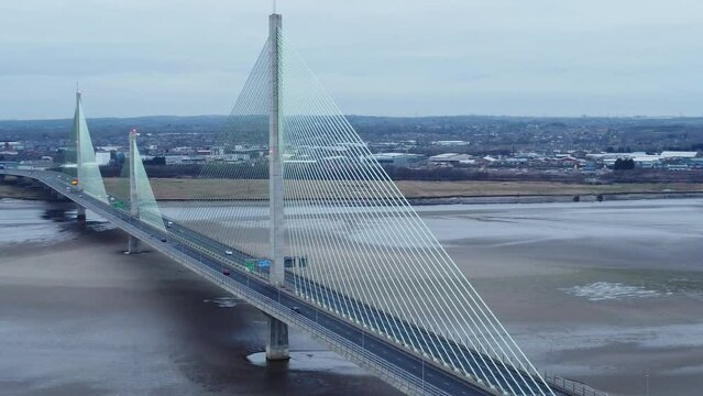 Aerial view Mersey Gateway cable stayed toll bridge traffic crossing River Mersey at low tide slow right dolly