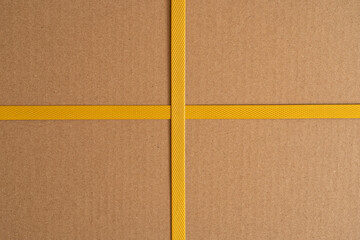 The side of the carton wrapped with yellow strapping tape. The tape crosses crosswise, forming four...