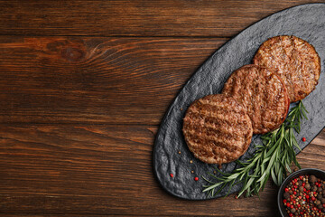 Slate plate with tasty grilled hamburger patties and seasonings on wooden table, flat lay. Space for text